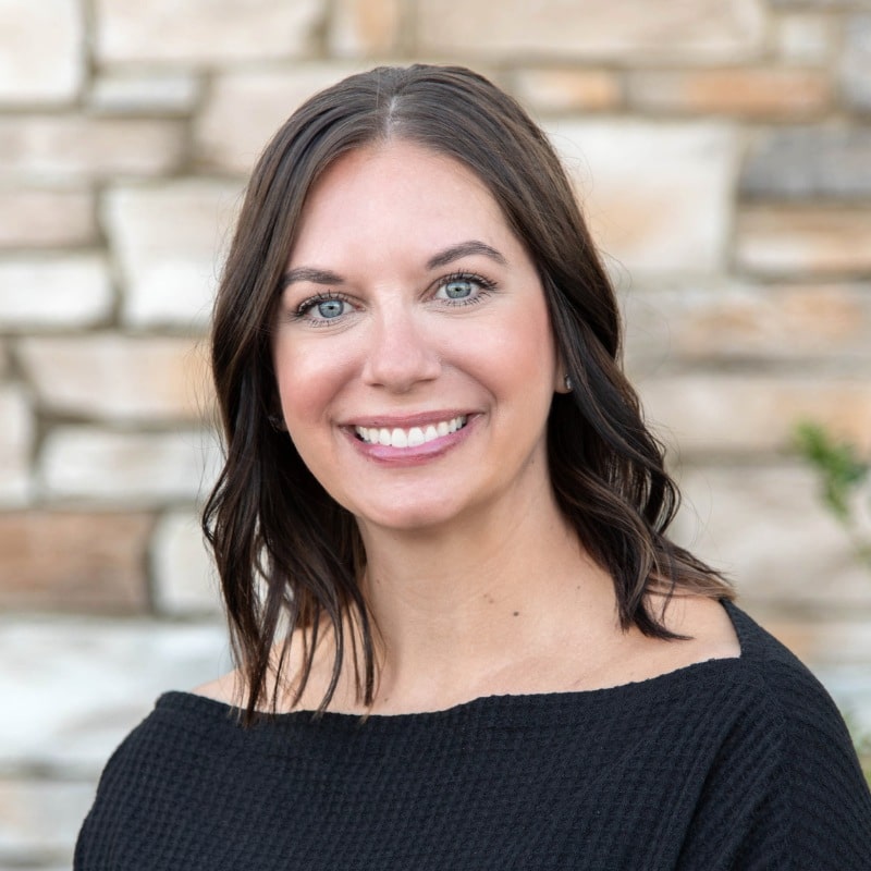 Ashley-treatment-coordinator-horton-orthodontics Smiling female team member posing outdoors in front of a stone wall.